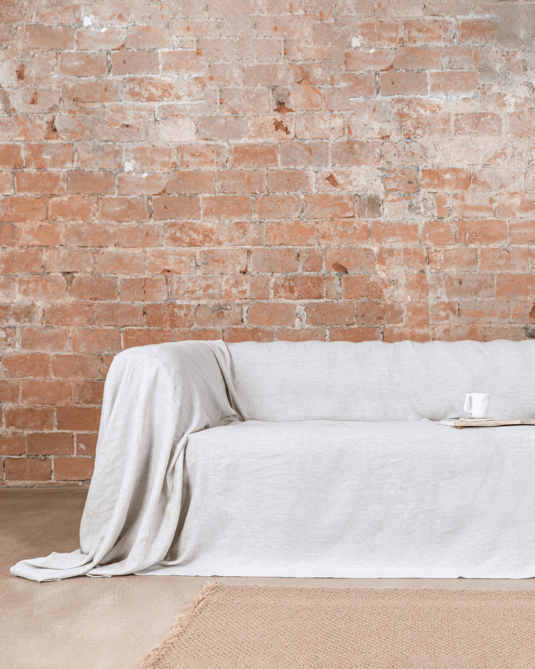 a couch covered with a white blanket in front of a brick wall
