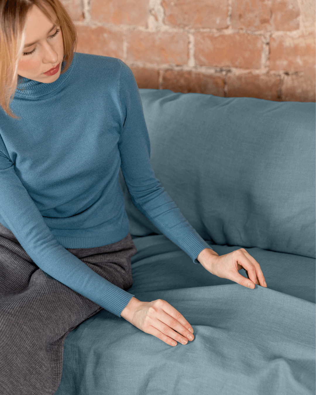 a woman sitting on a blue couch with a brick wall behind her