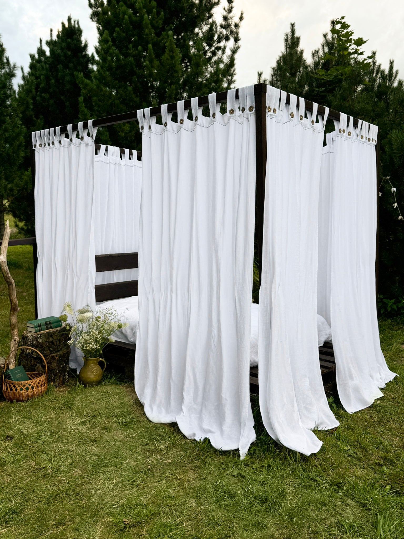 a bed with white curtains on it sitting in the grass