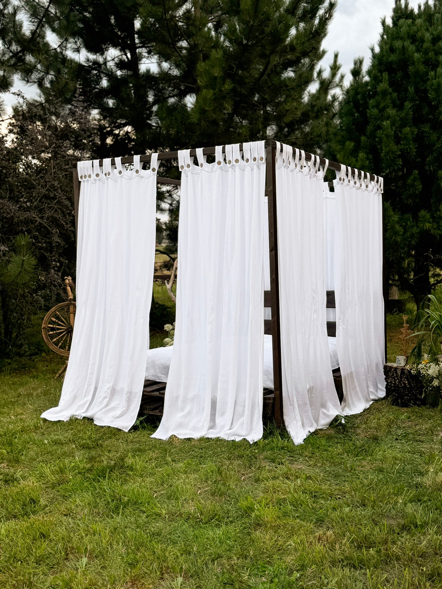 a white curtained bed sitting in the middle of a lush green field