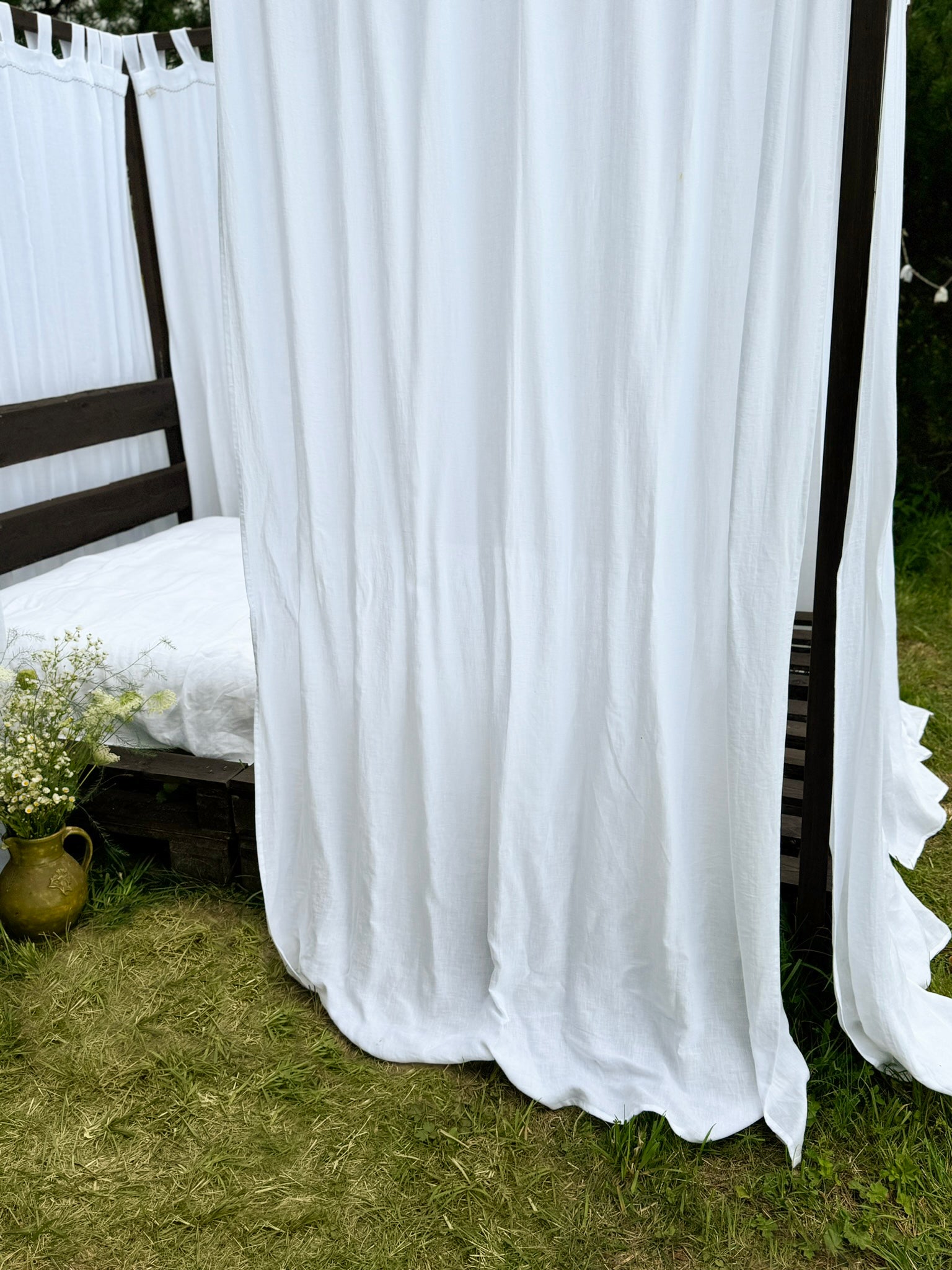 a bed sitting in the grass next to a white curtain