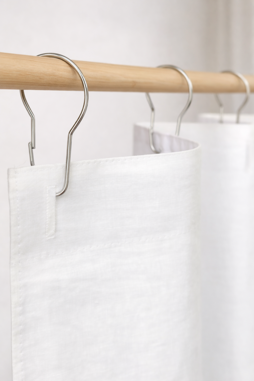 White linen curtains hanging on a wooden rack with metal hooks.