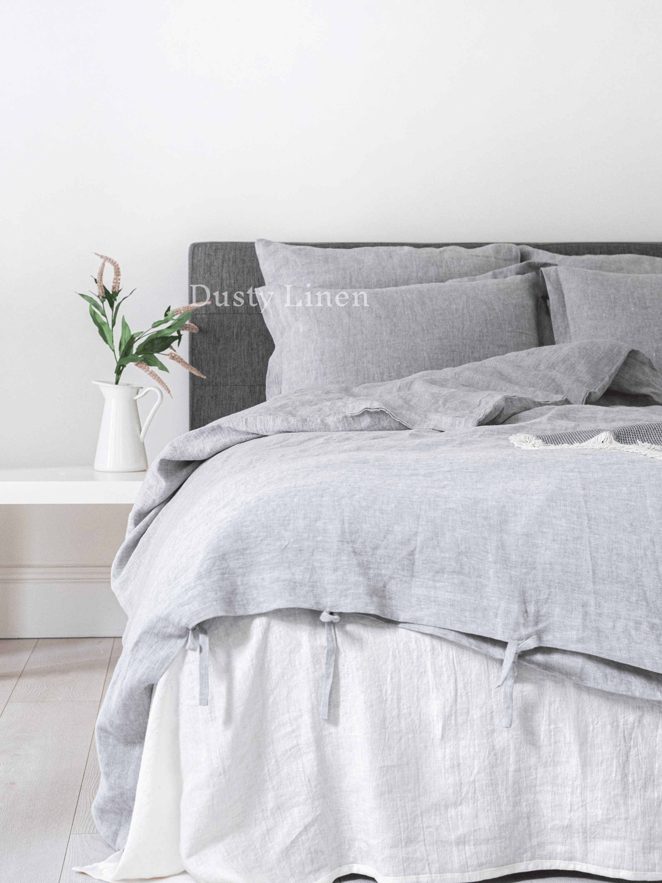 a bed with a gray comforter and a white vase with flowers