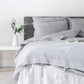 a bed with a gray comforter and a white vase with flowers