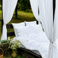 a bed with white sheets and curtains in a field