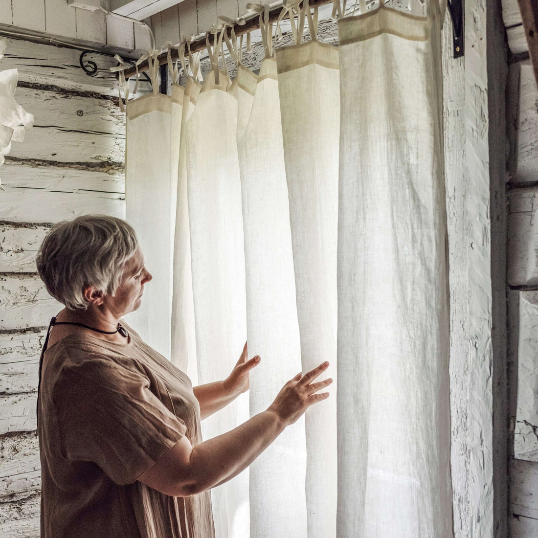 Woman measuring or adjusting a linen curtain beside a window