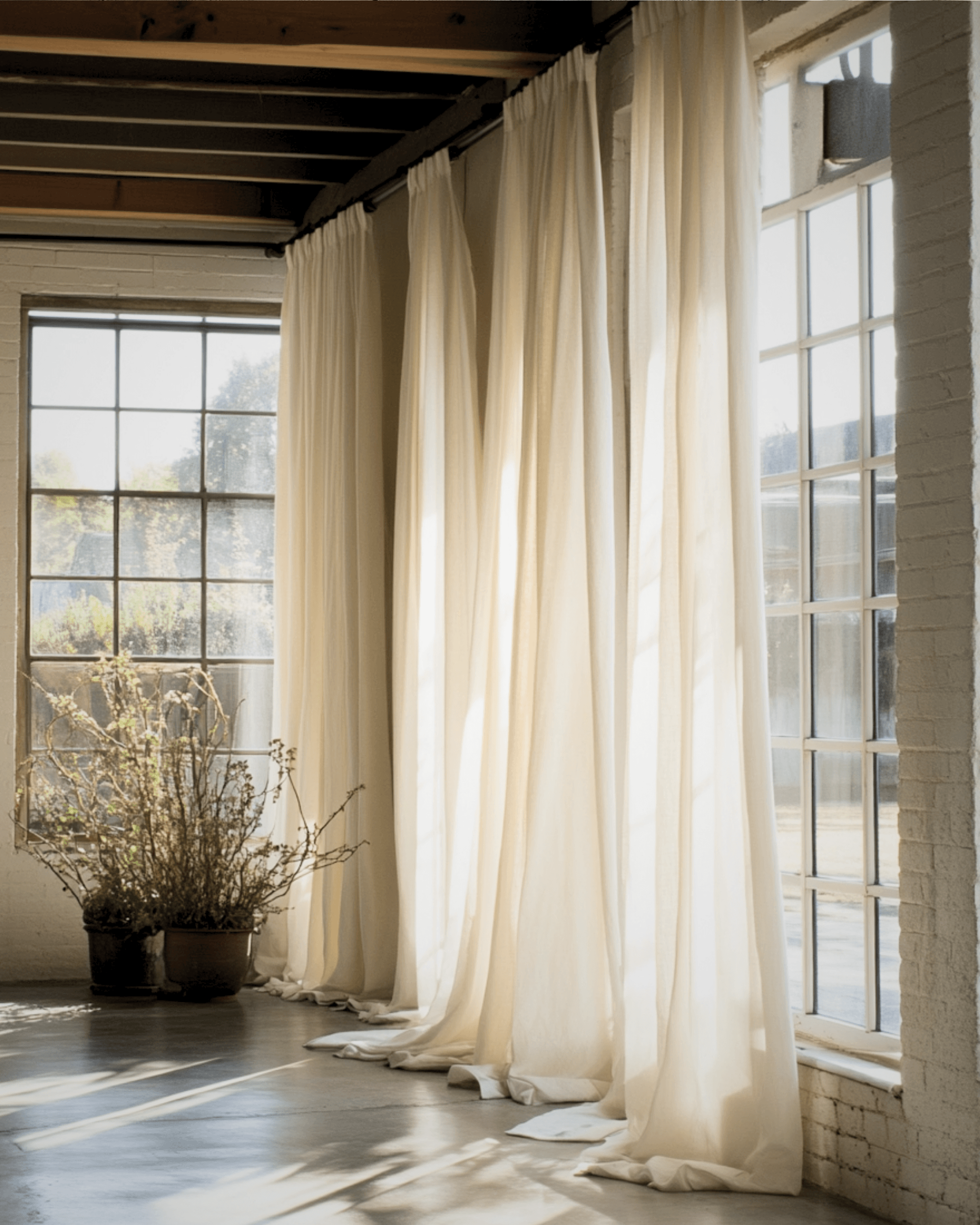 Extra long linen curtains pooling by tall windows in a bright room with soft daylight.