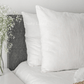 a white bed topped with pillows and a vase filled with flowers