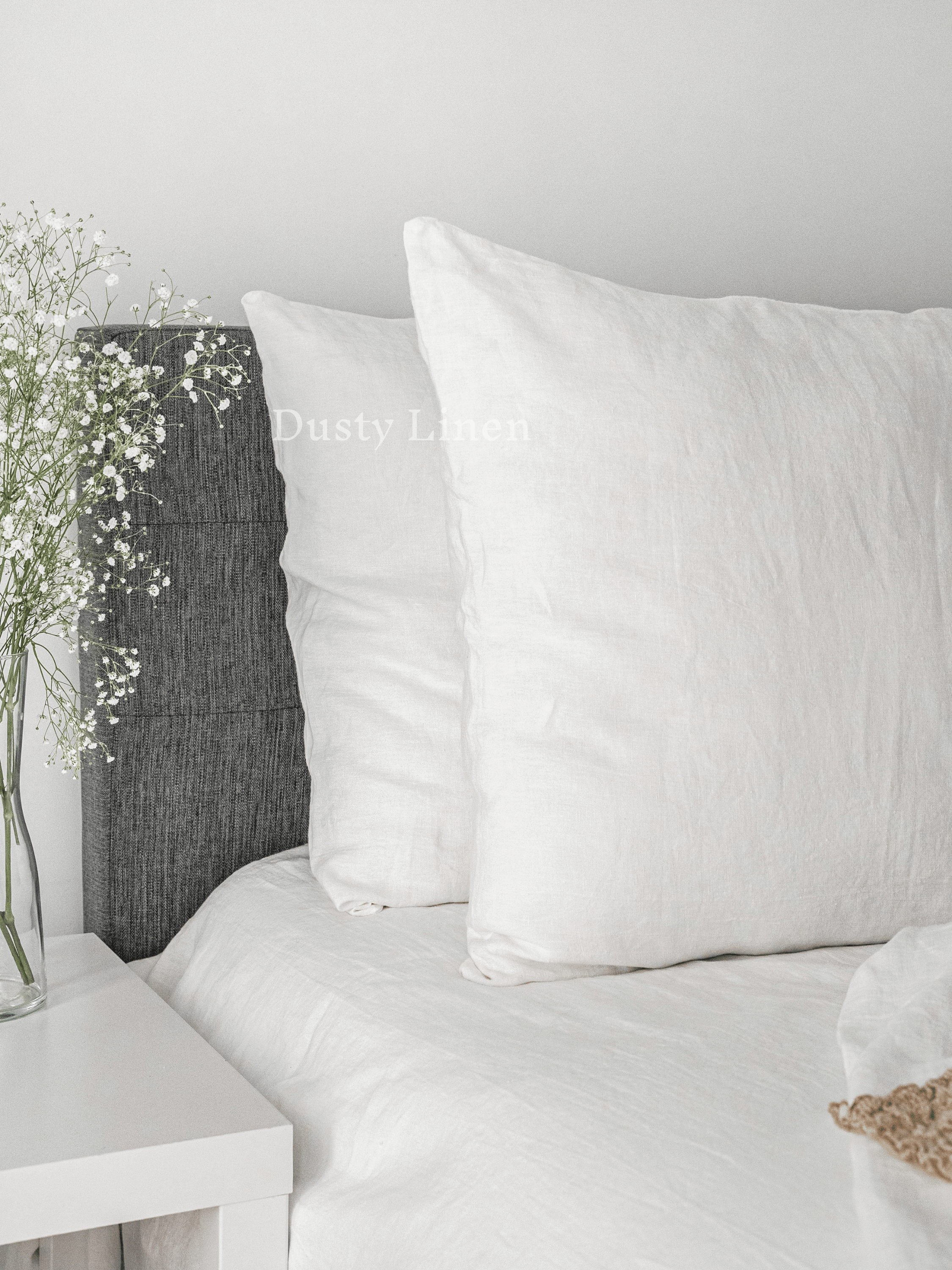 a white bed topped with pillows and a vase filled with flowers