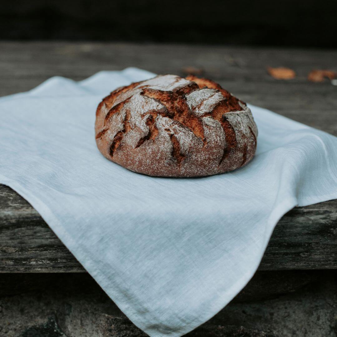 Linen tea towel with artisan loaf on a dark surface
