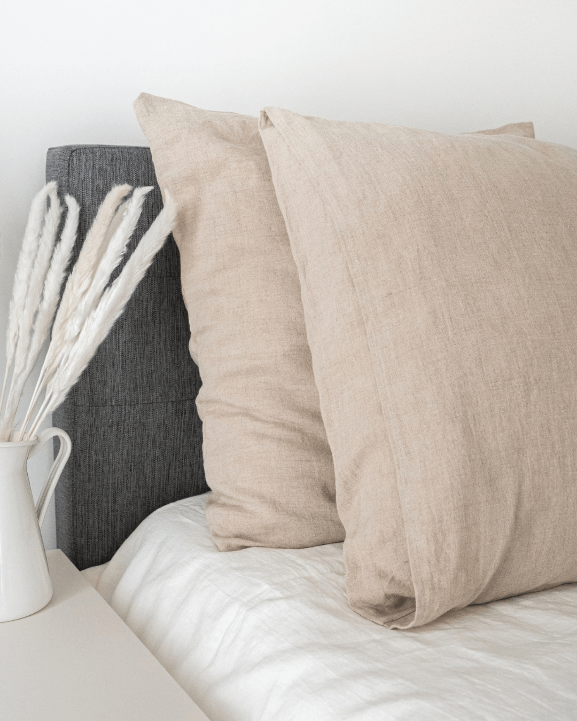 Two minimalist linen pillowcases on natural bed with dried flower arrangement