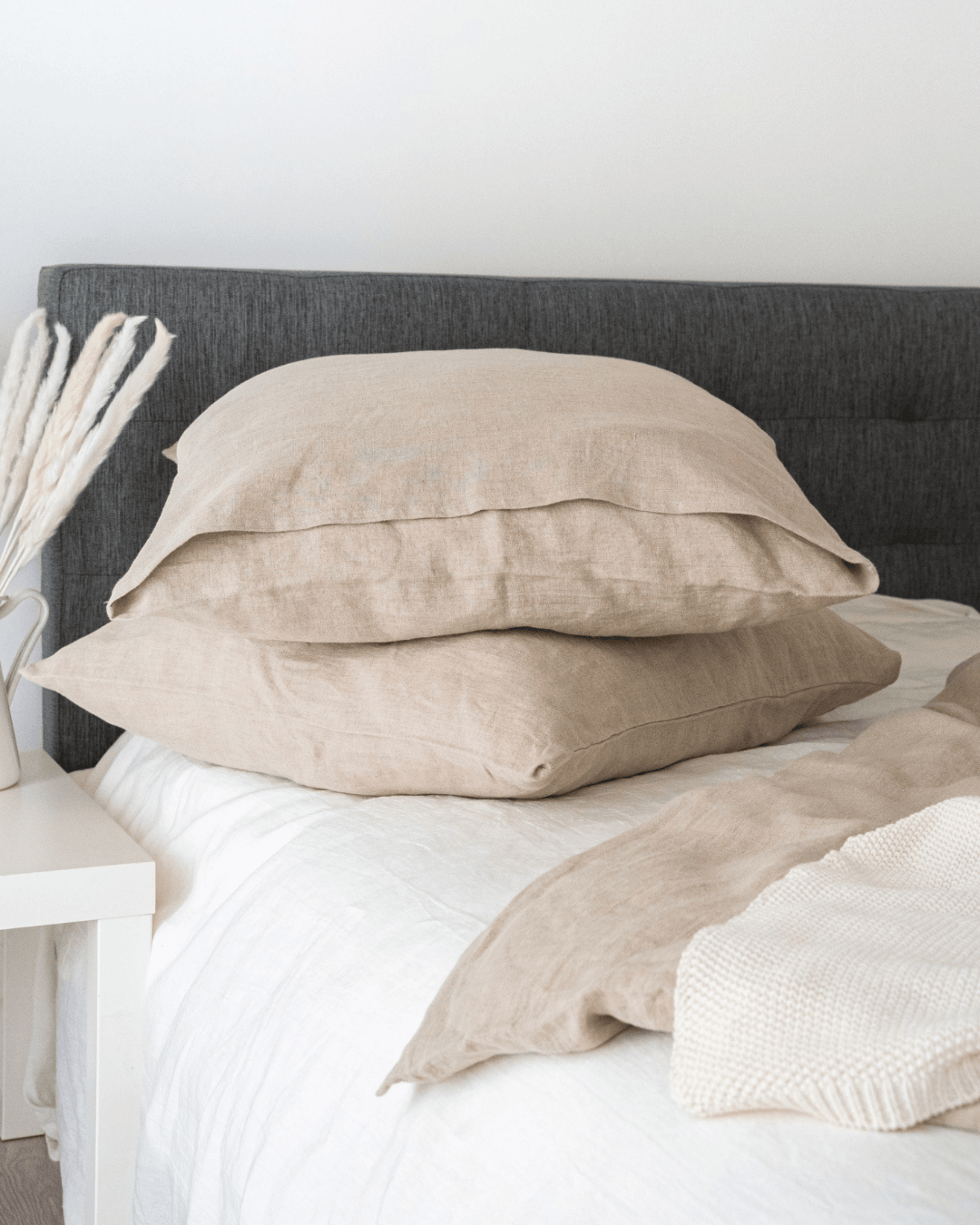 Minimalist linen pillowcases on bed with linen blanket and wooden nightstand