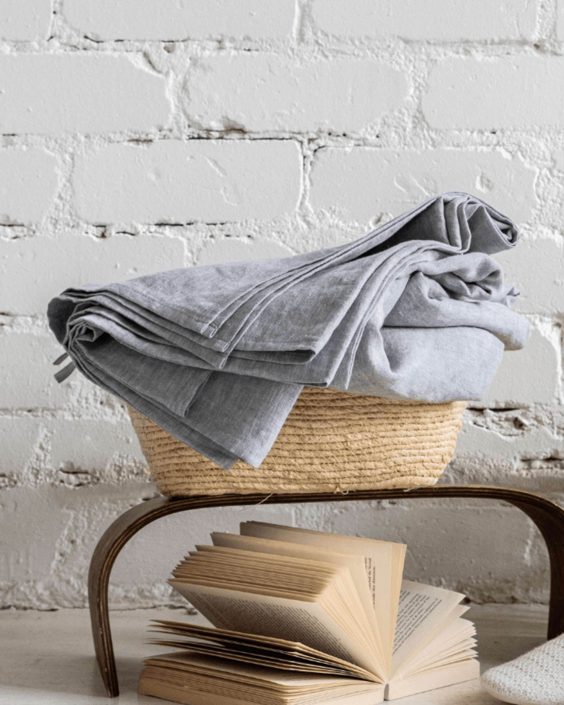 Linen flat sheet folded on bedside table with books and basket