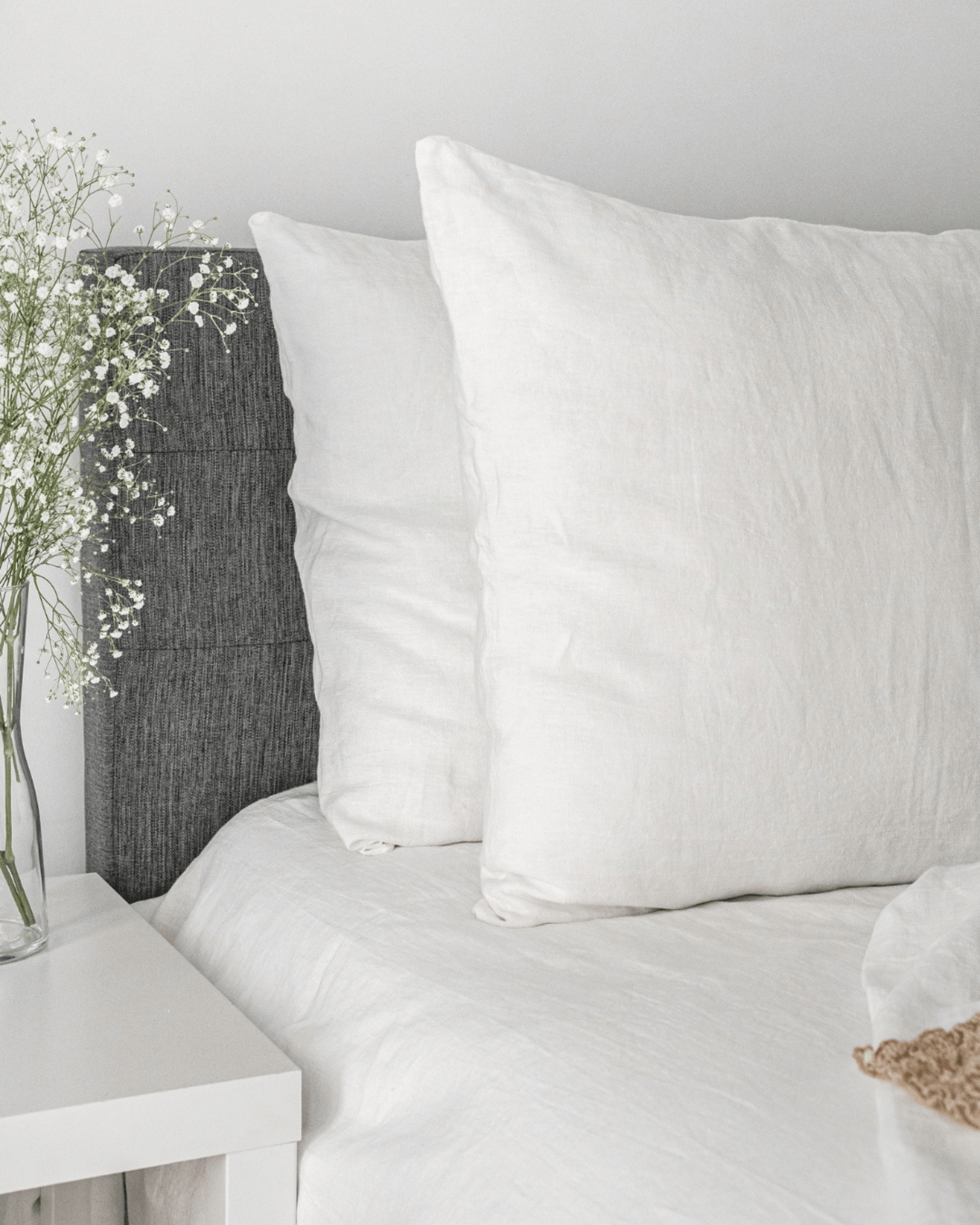 Off white minimalist linen pillowcase on styled bed with flowers