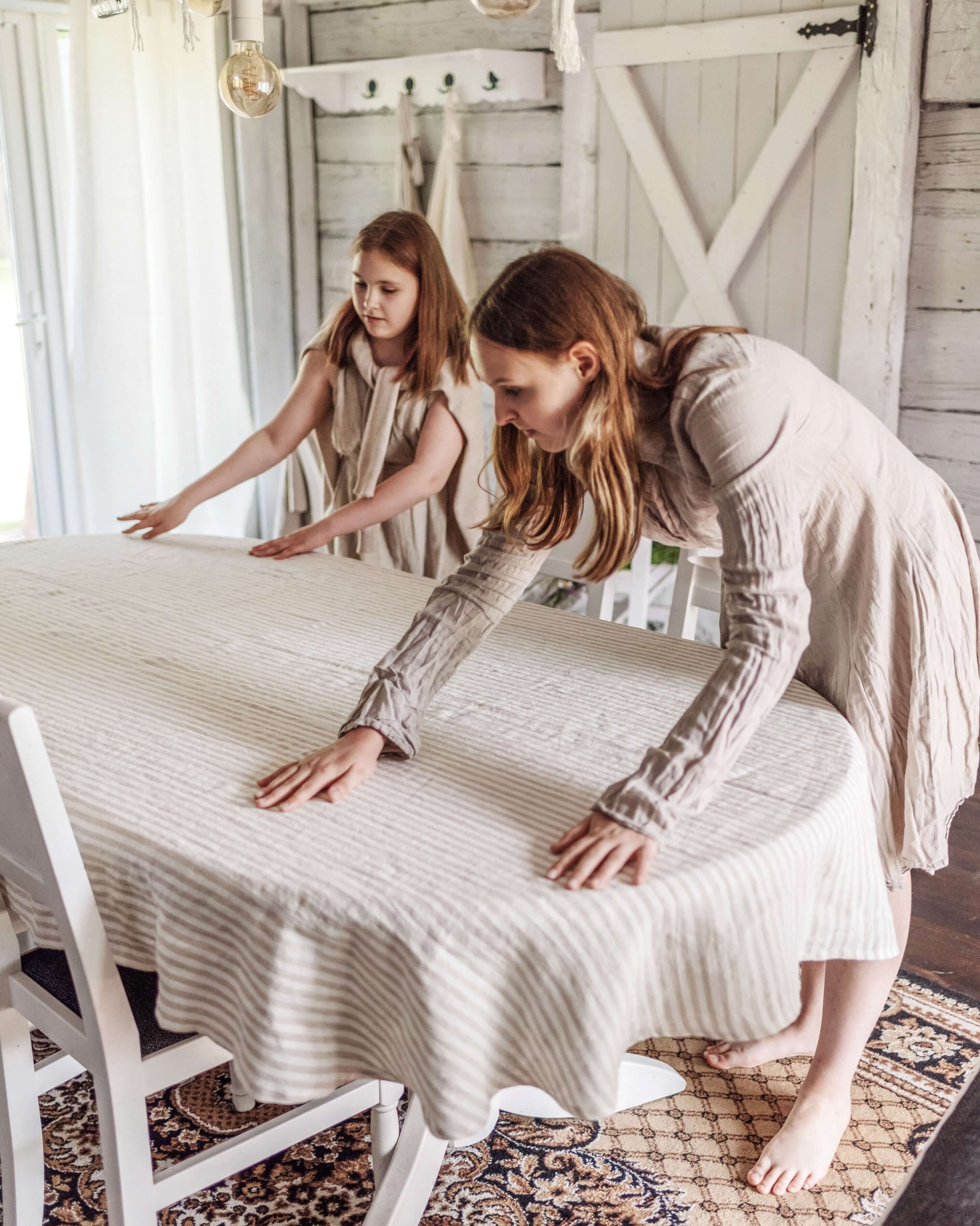 Woman styling oval linen tablecloth on dining table