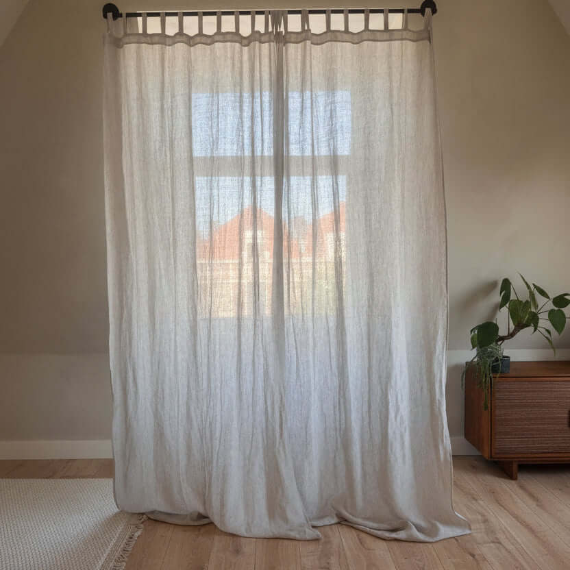 Sheer linen curtains hanging on a bedroom window with natural light