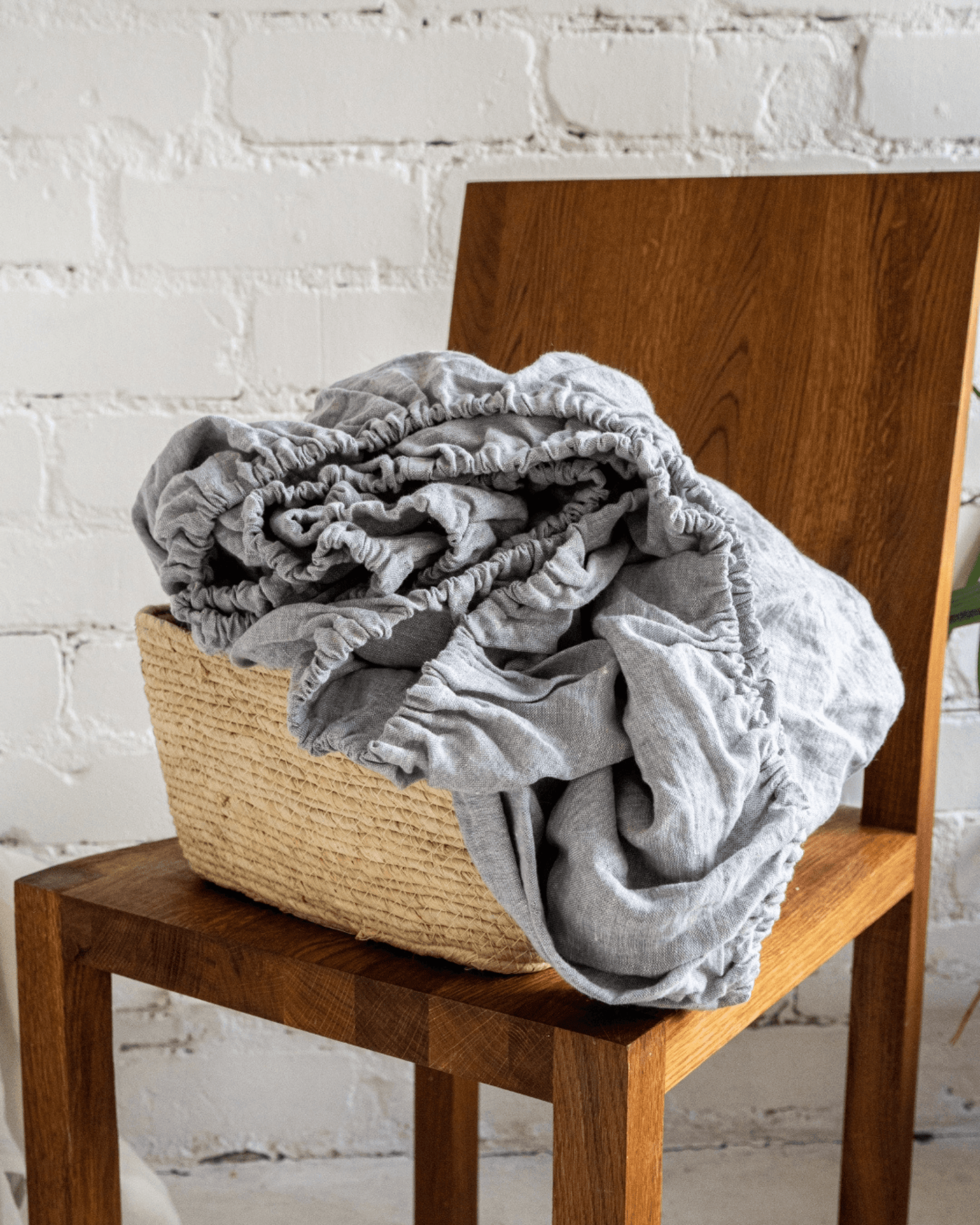 Linen fitted sheet on bed, armchair with linen blanket in background
