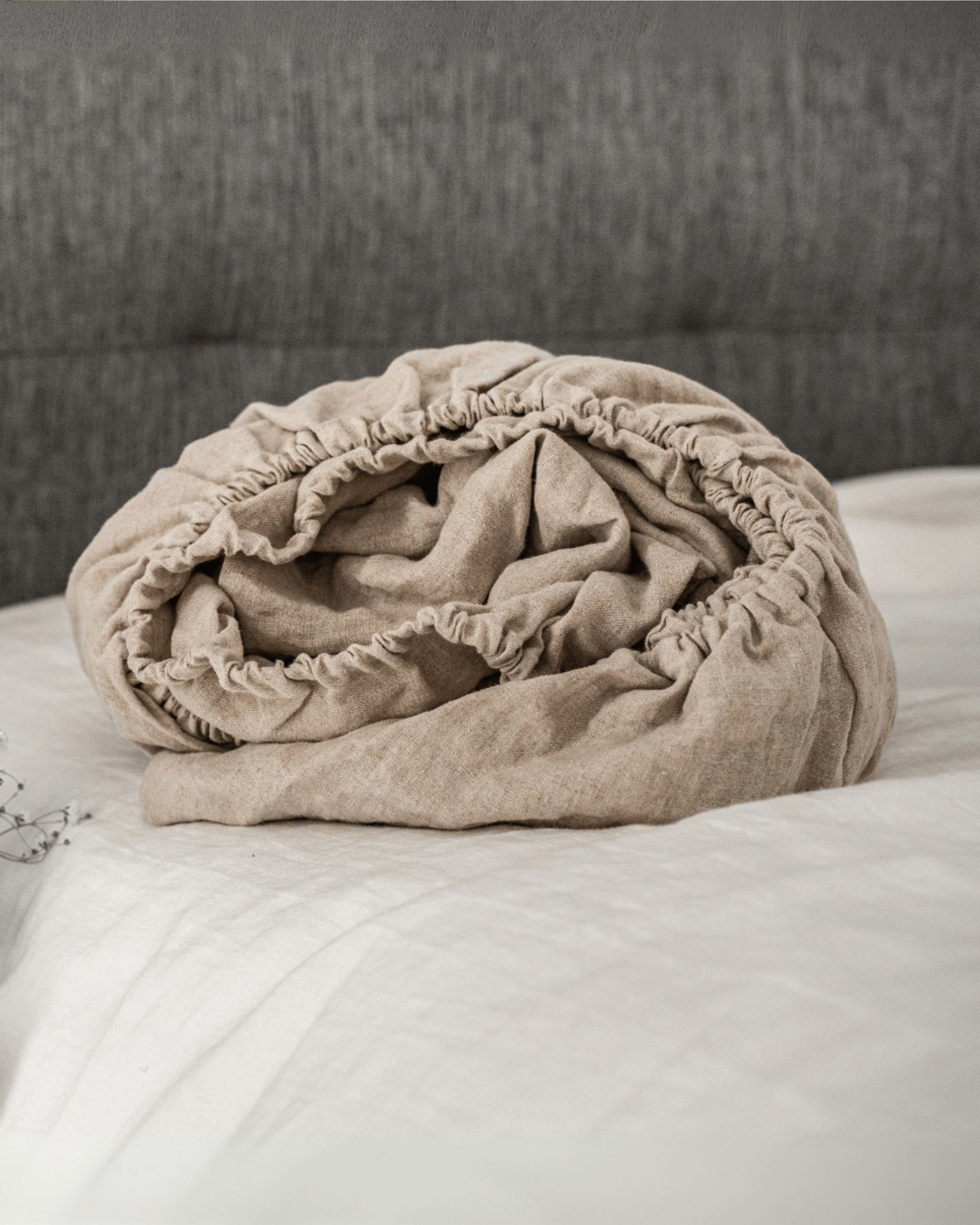 Linen fitted sheet on bed styled with linen blanket and floral vase