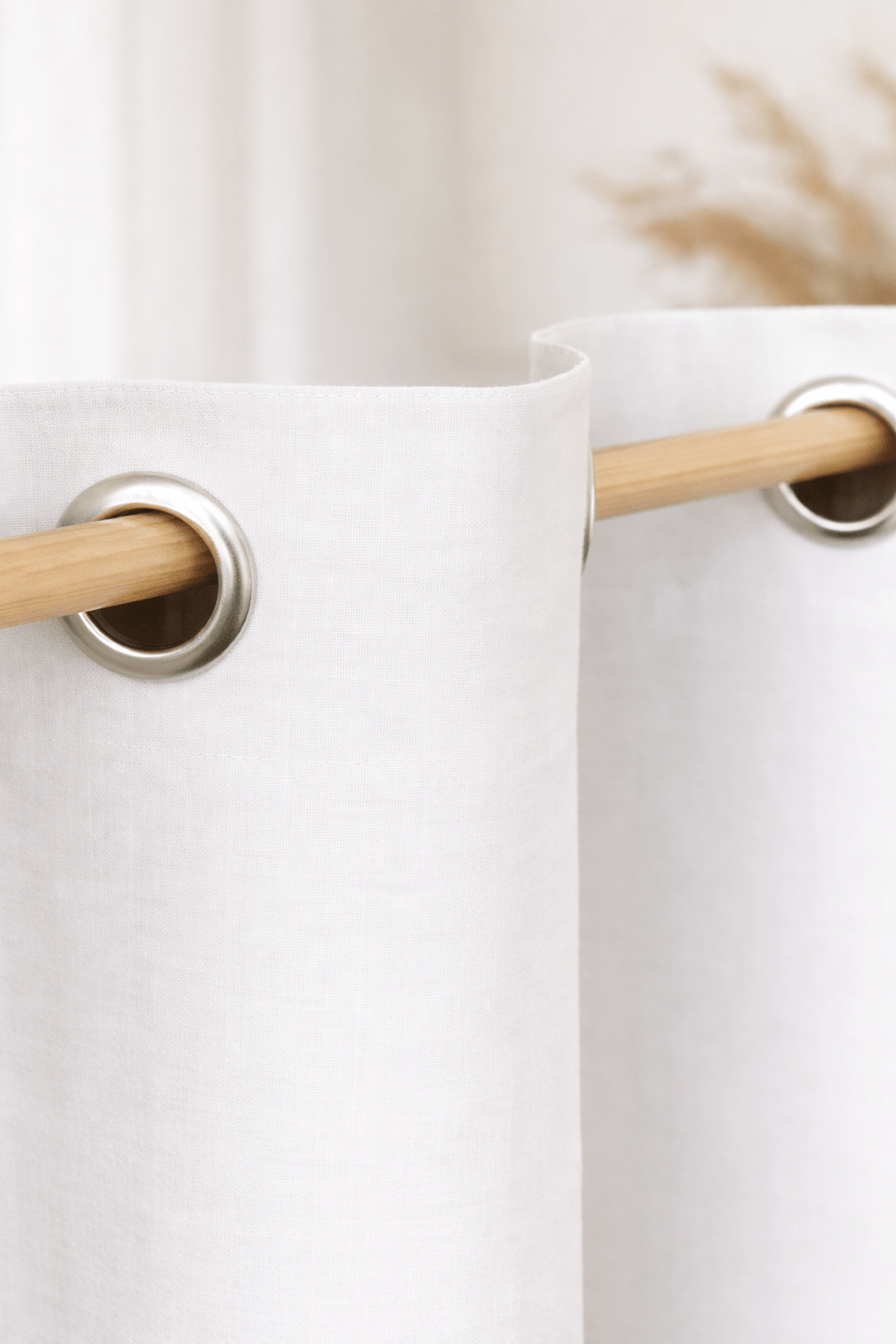 White linen curtain with grommet top detail on a wooden rod