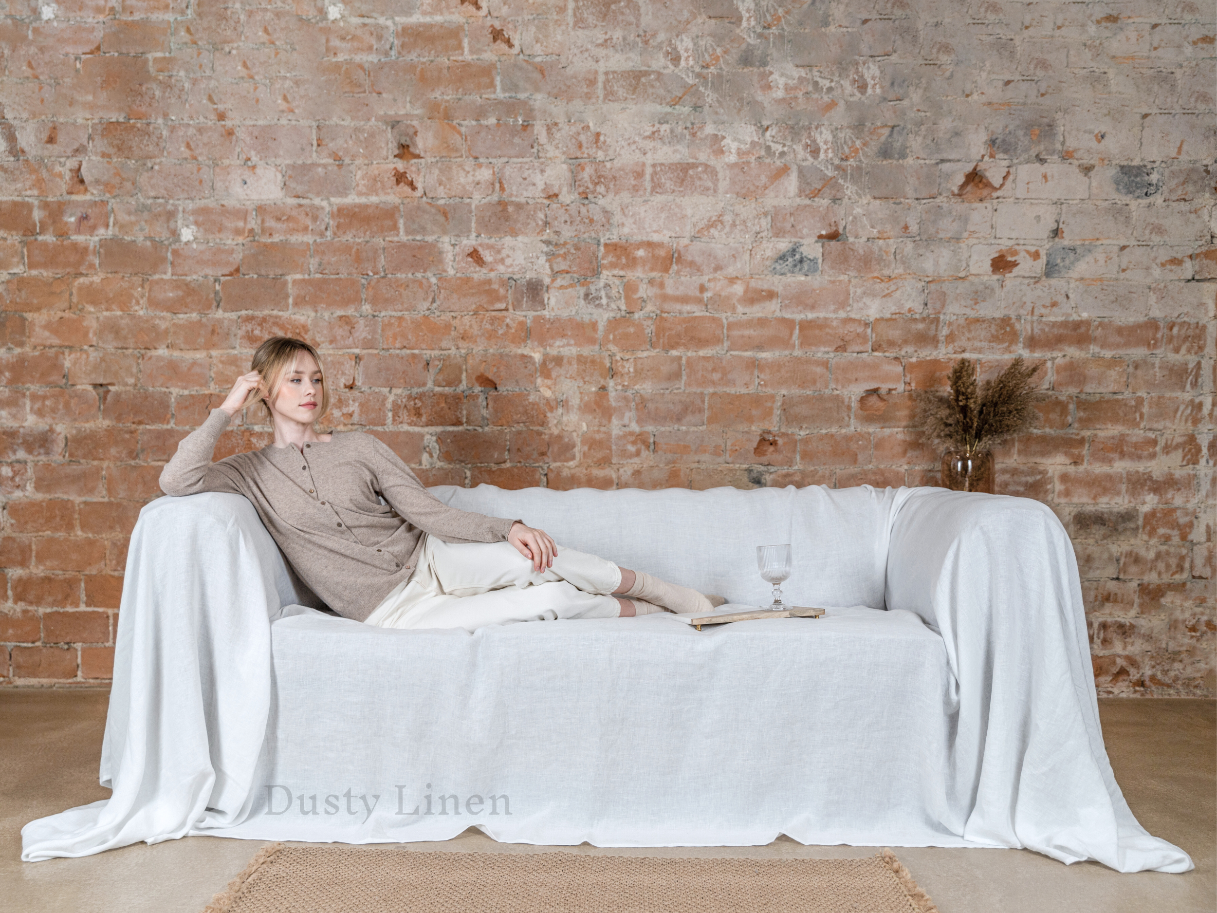 a woman sitting on a white couch in front of a brick wall