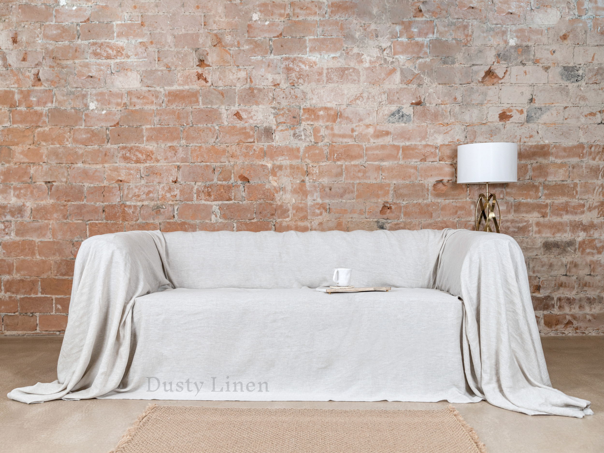 a couch covered with a white blanket in front of a brick wall