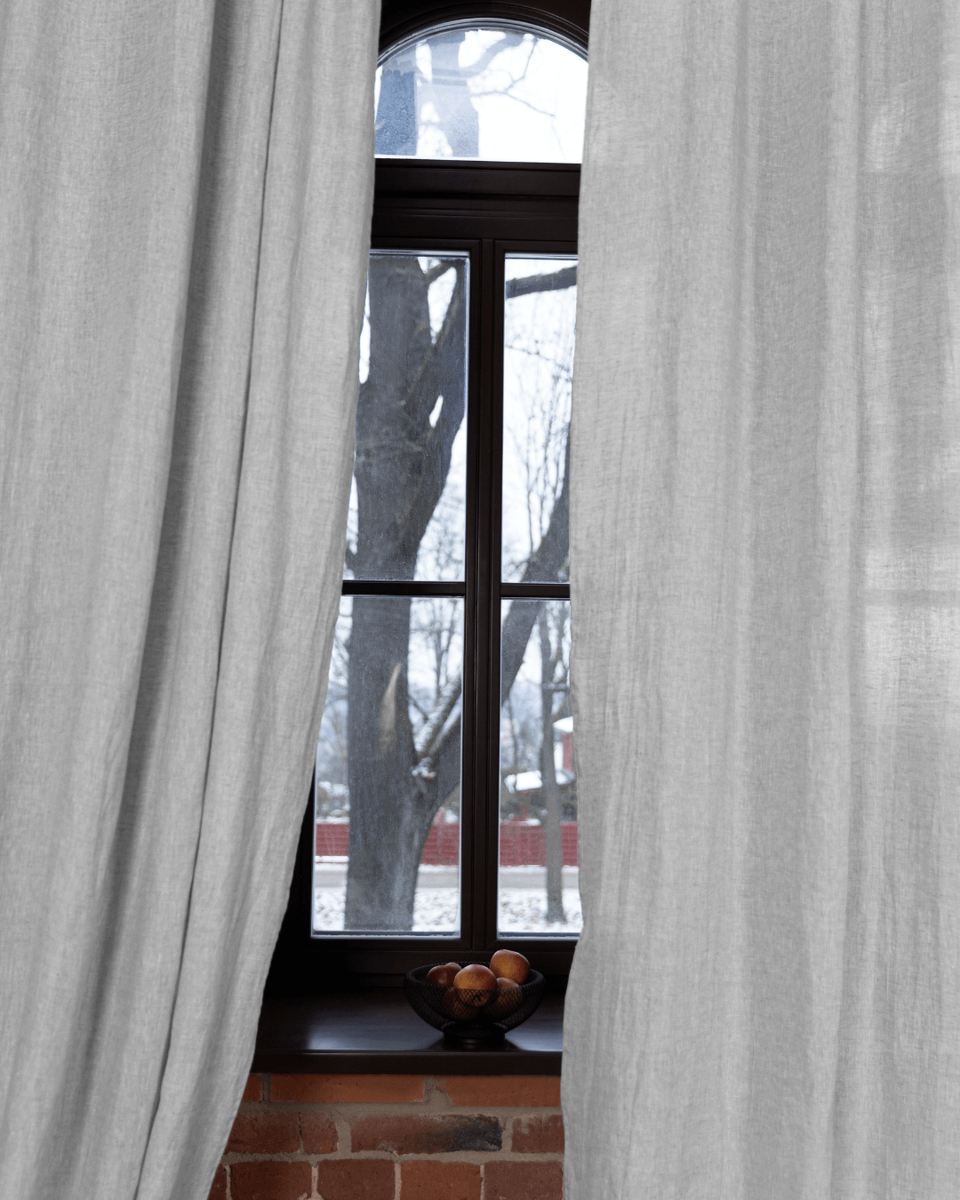 a window with a curtain and a bowl of fruit in front of it