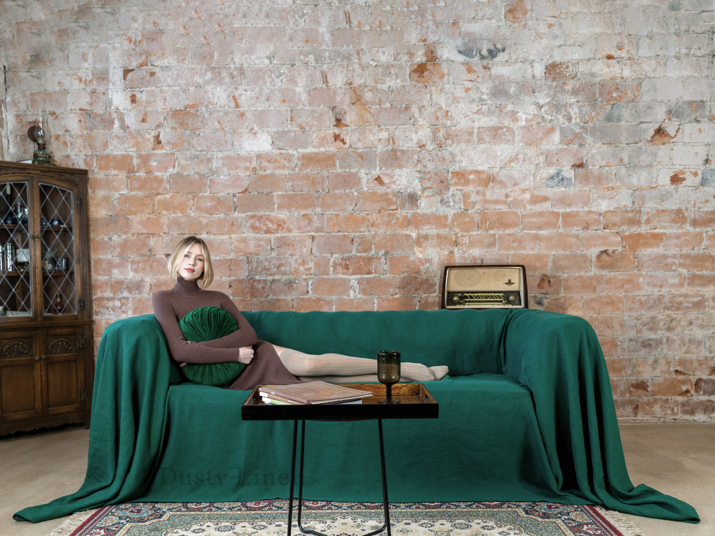 a woman sitting on a green couch in front of a brick wall