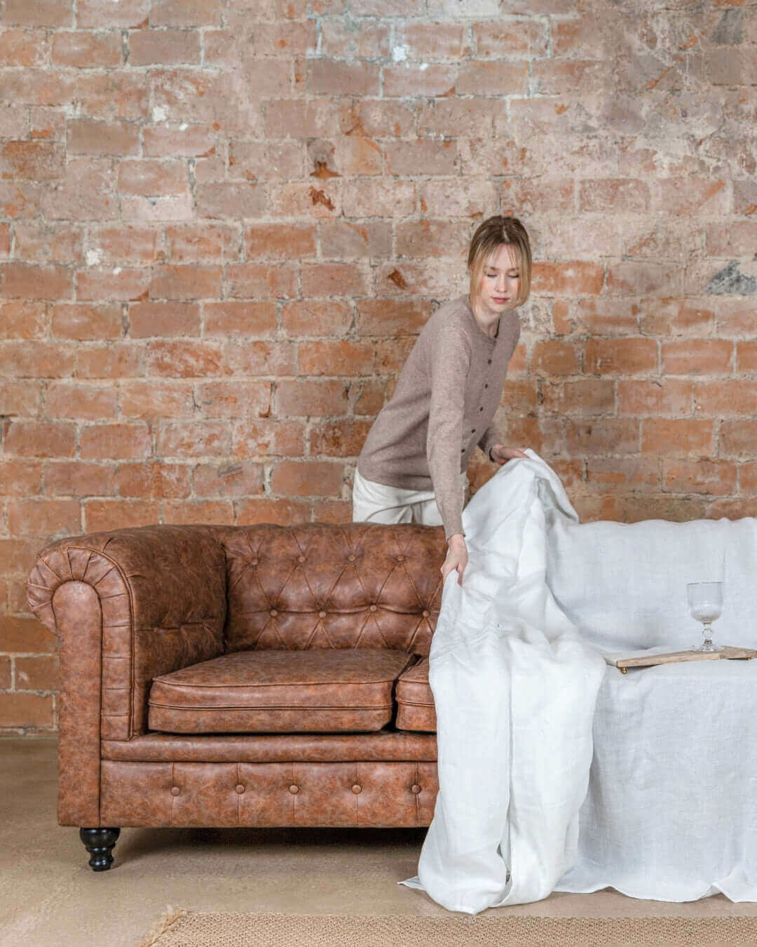 a woman standing next to a couch covered in a white linen blanket