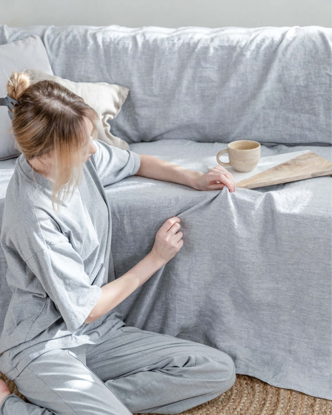 a woman sitting on a couch holding a book. Behind linen sofa cover in light gray color