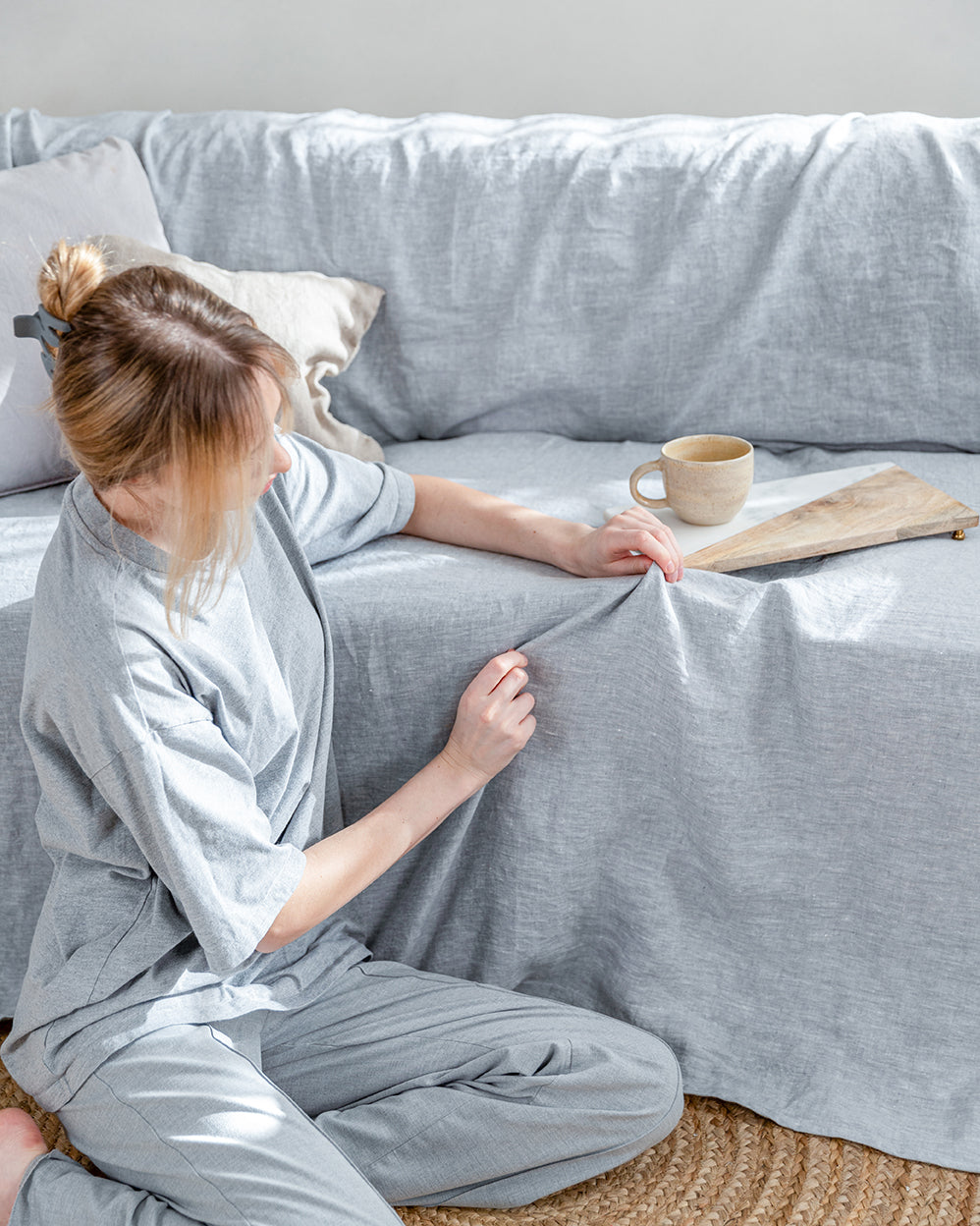 a woman sitting on a couch holding a book. Behind linen sofa cover in light gray color