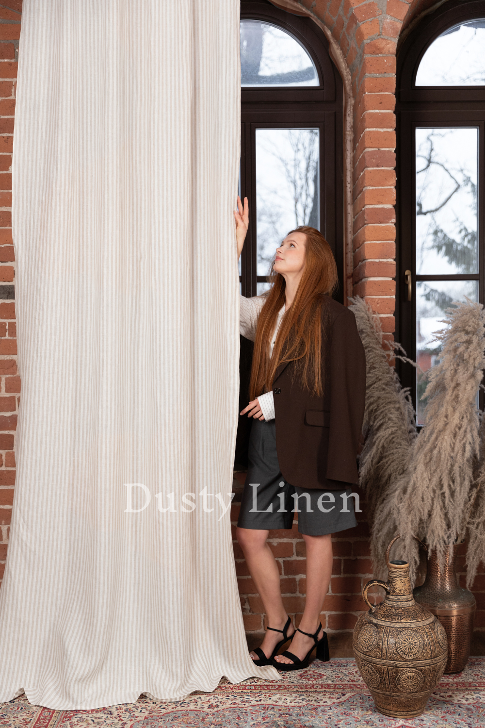 a woman standing next to a window in front of a curtain