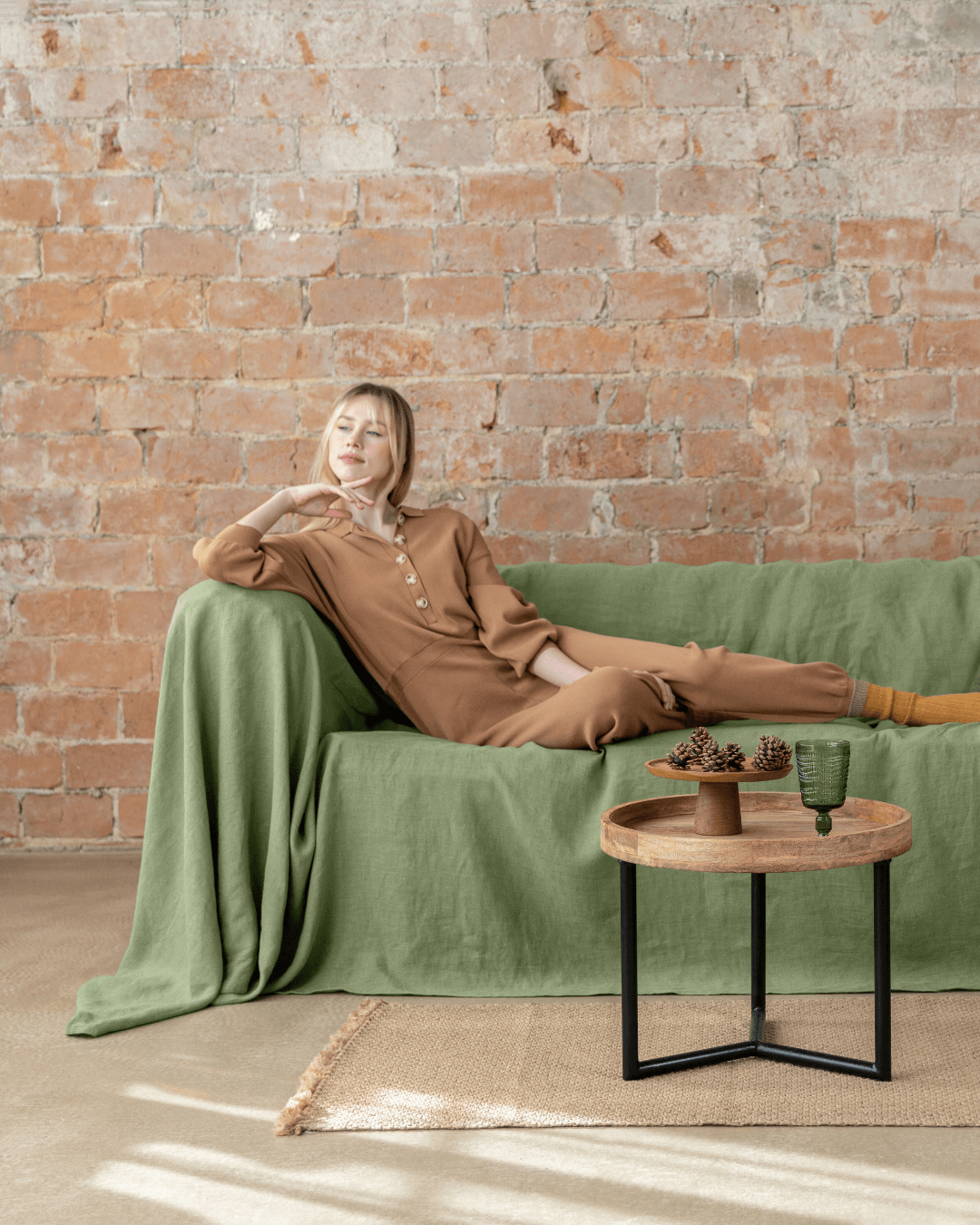 a woman sitting on a green couch in front of a brick wall