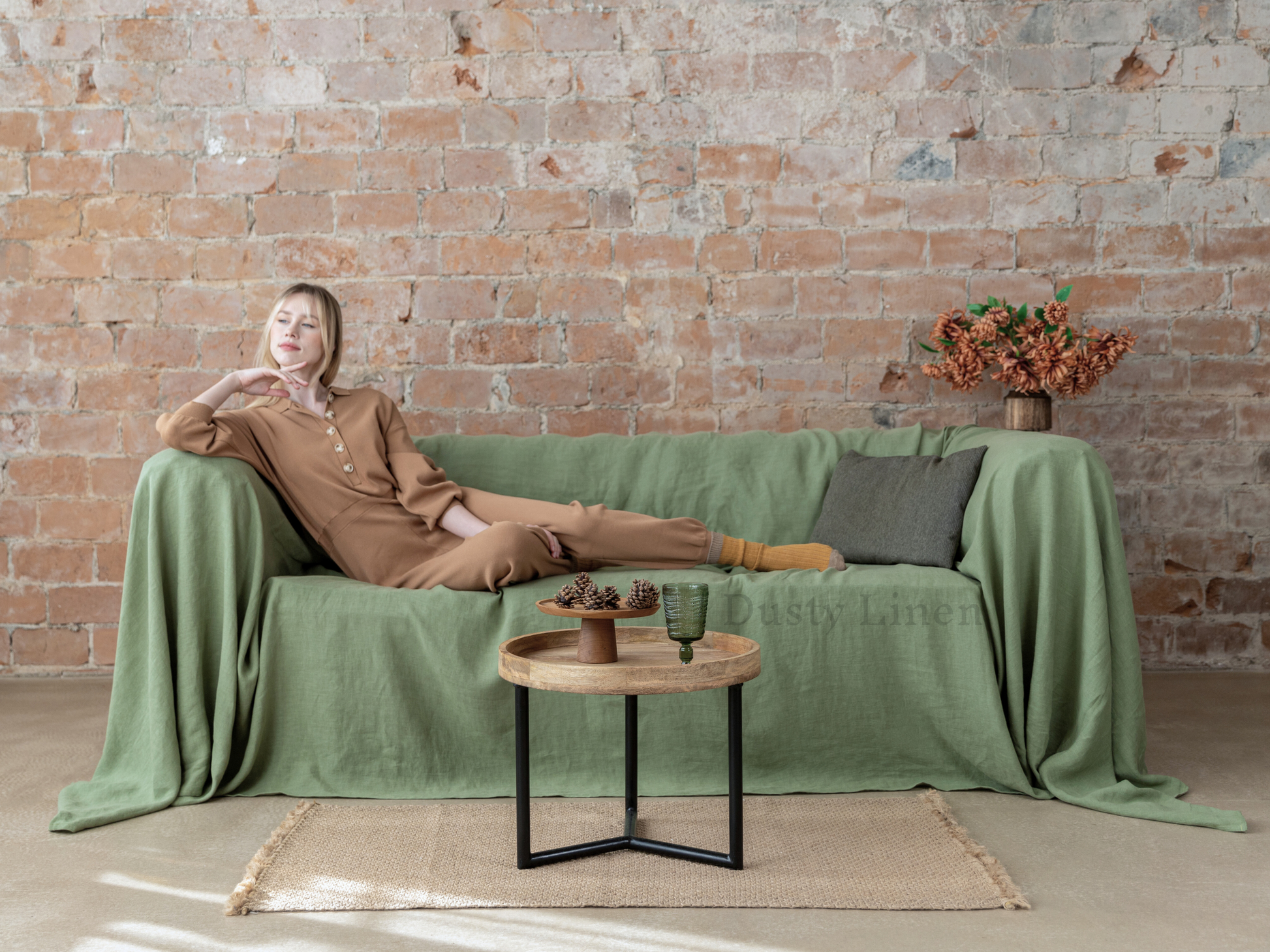 a woman sitting on a green couch in front of a brick wall