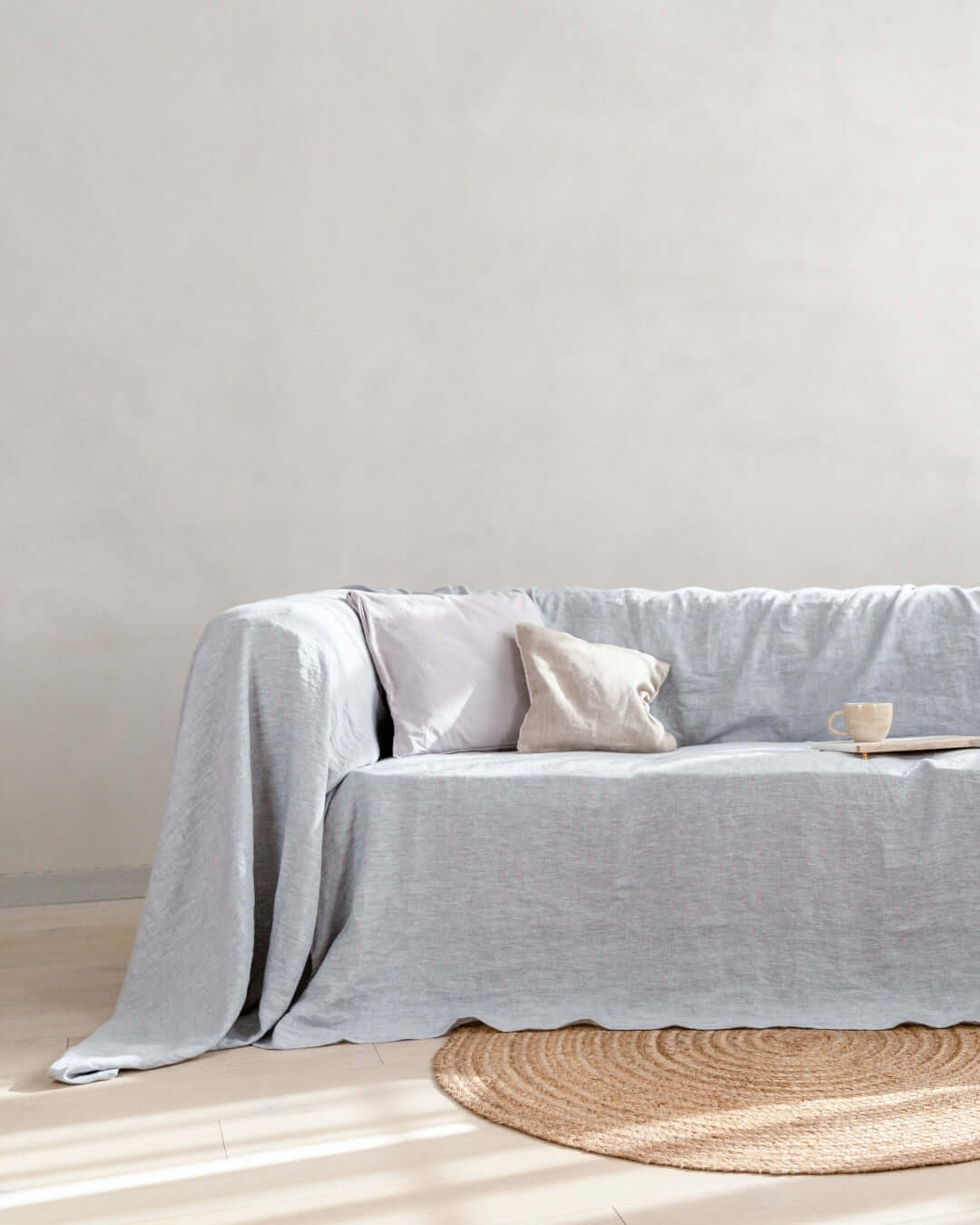 a woman sitting on top of a couch in a living room. Linen couch cover in light gray color