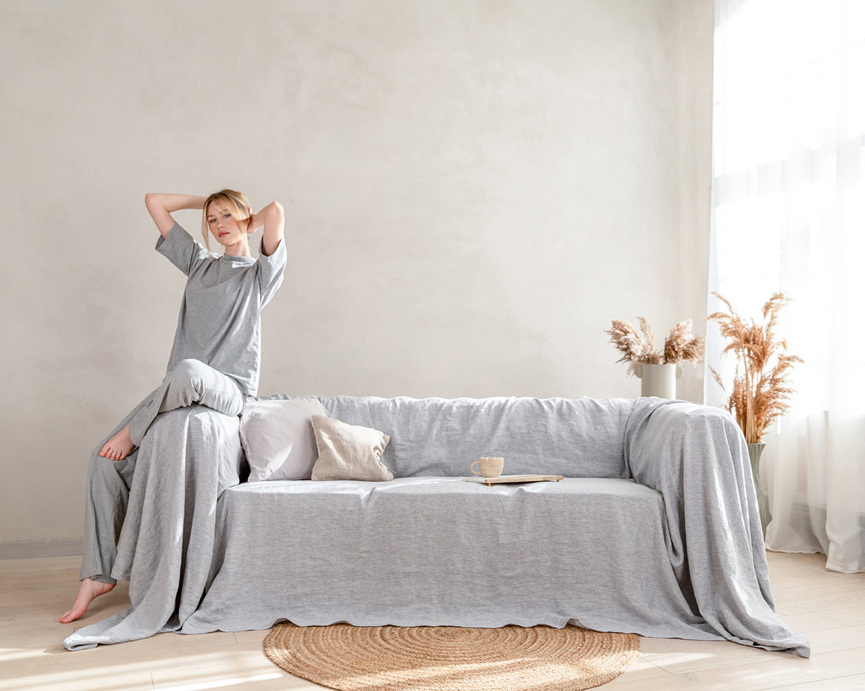 a woman sitting on top of a couch in a living room. Linen couch cover in light gray color