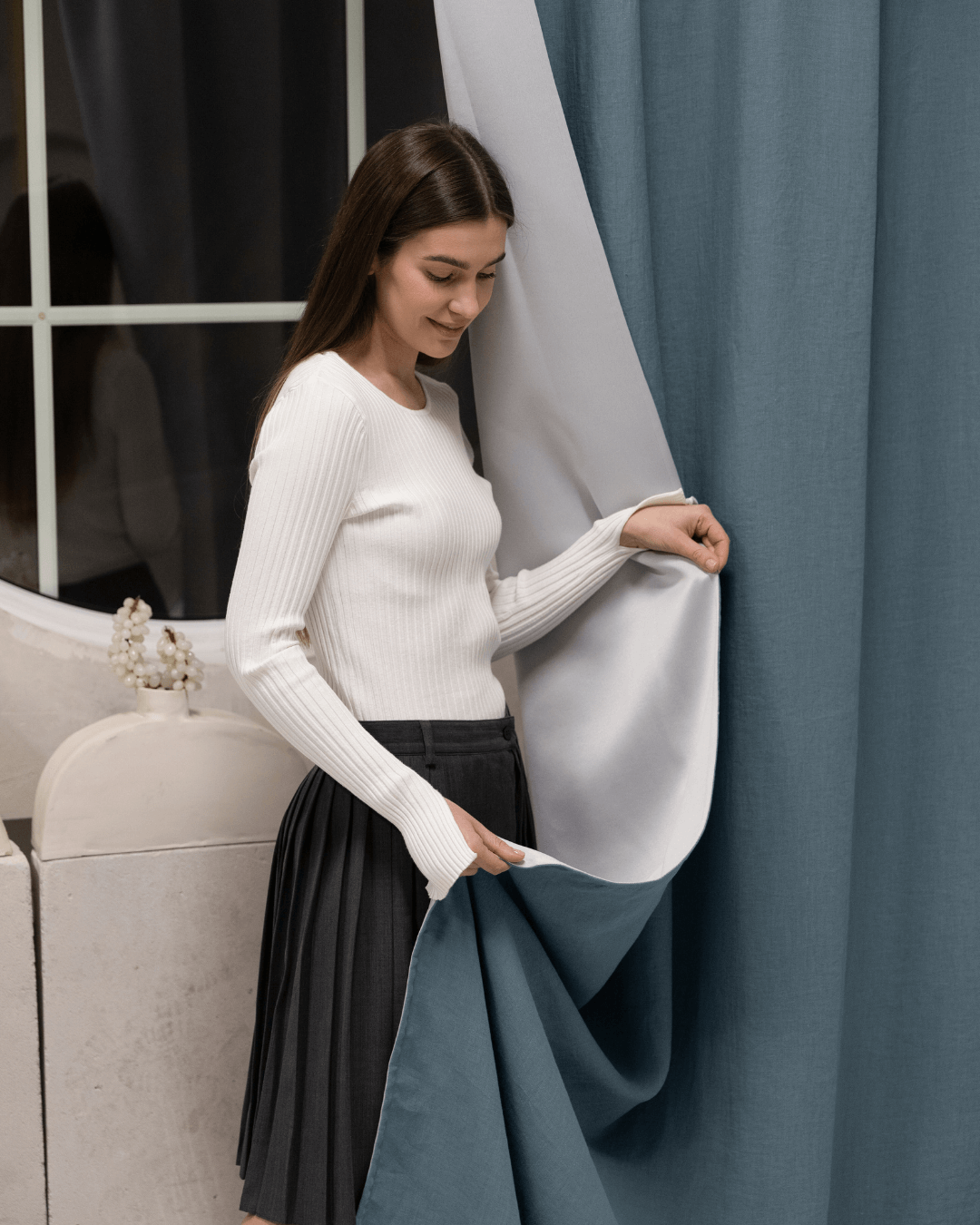 Woman opening gray blue linen blackout curtain at window