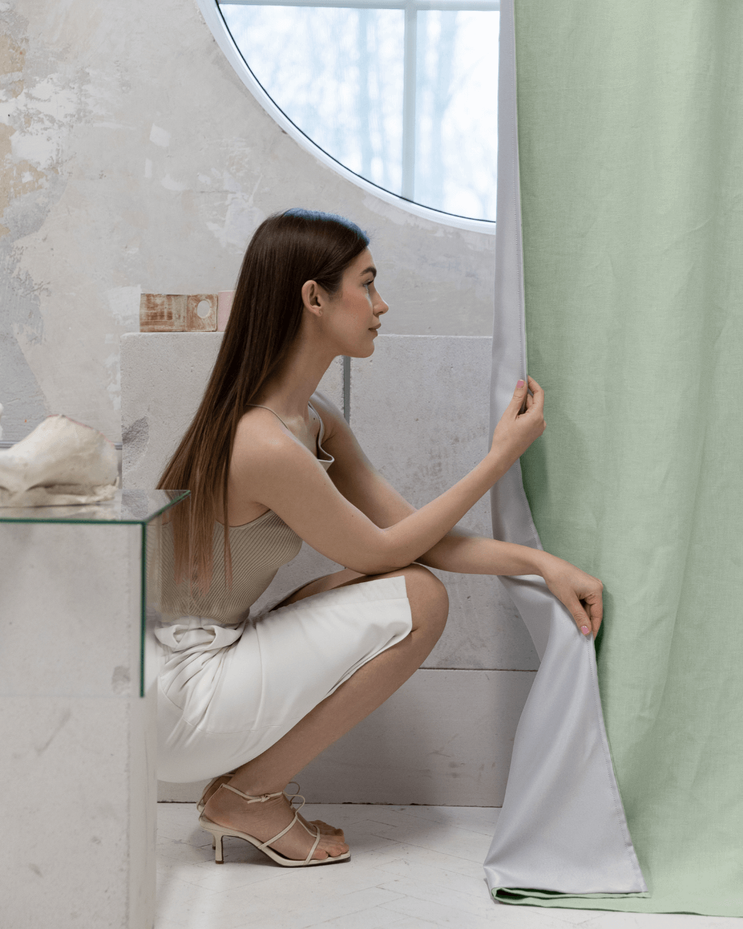 Woman seated on floor beside sage green linen blackout curtains
