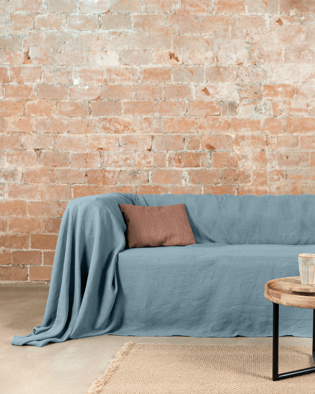 Gray blue linen couch cover draped on sofa next to side table