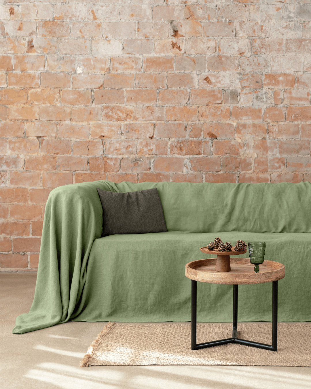 Khaki green linen couch cover on sofa next to brick wall, full view