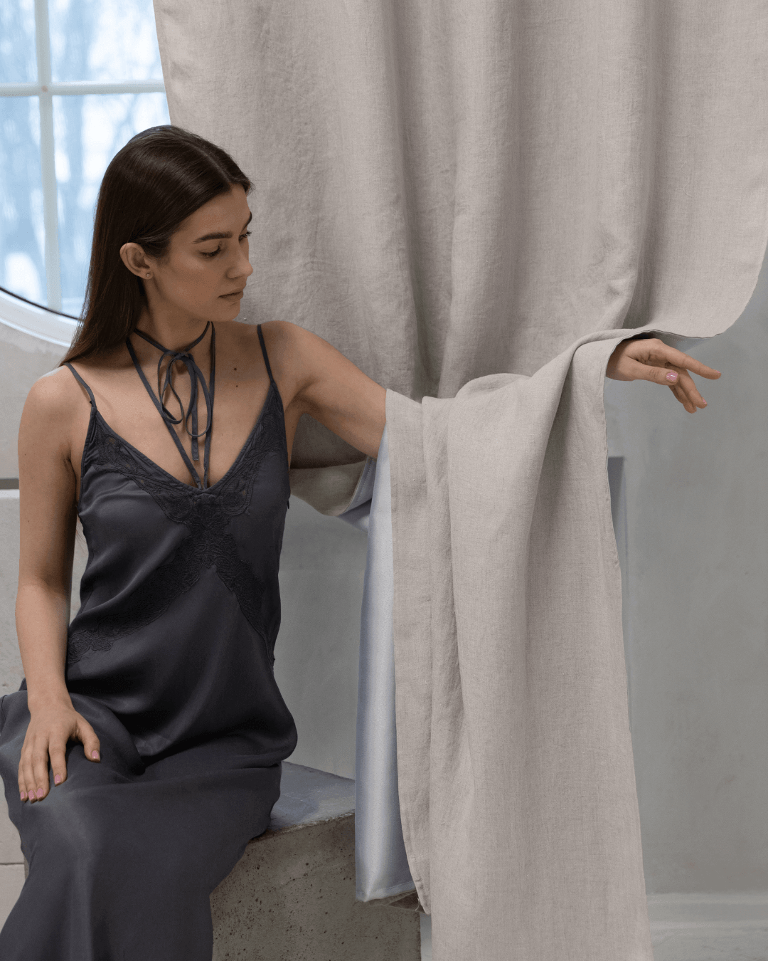 Woman on window ledge beside natural light linen blackout curtain panel