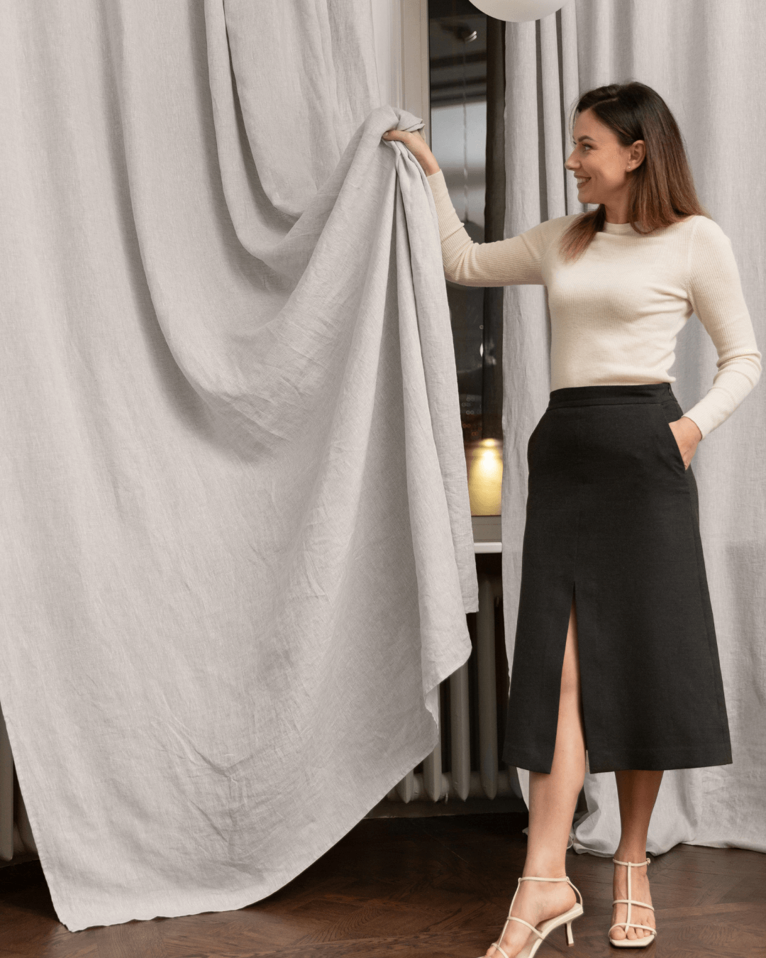 Woman beside natural light linen curtain panel, full length drape view