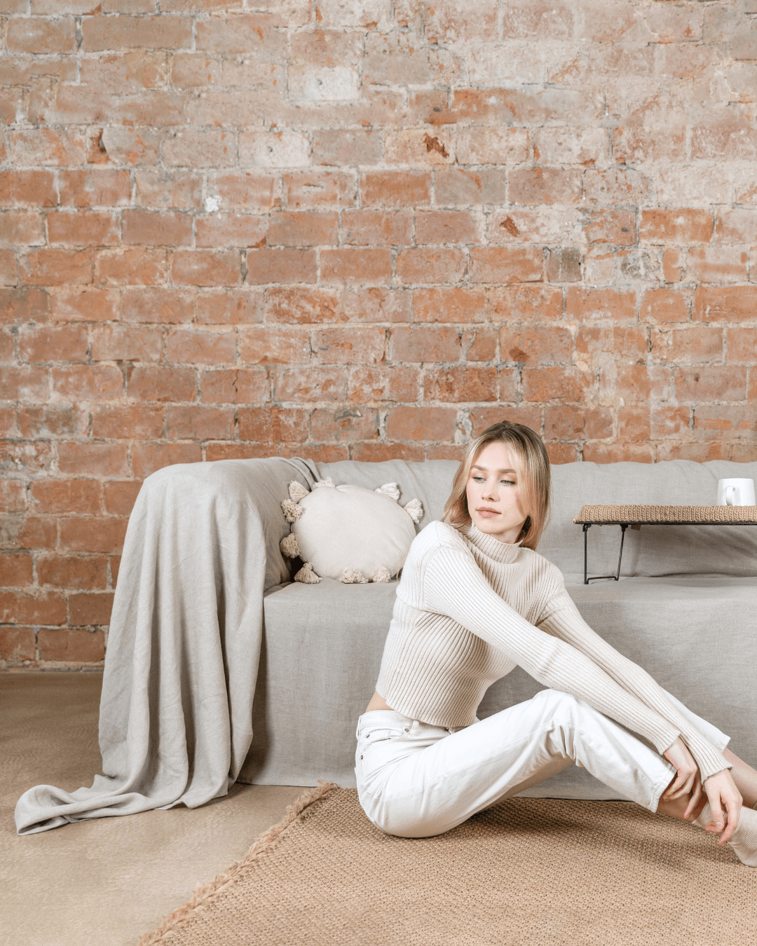 Woman sitting on rug in front of sofa with natural linen sofa cover