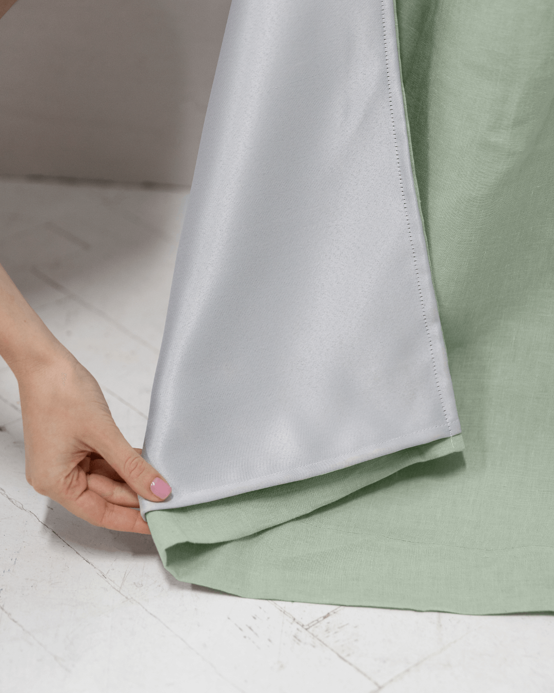 Woman holding edge of sage green linen blackout curtain panel