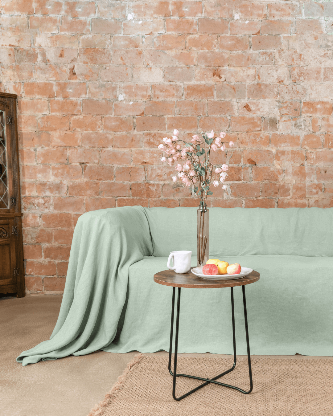 Sage green linen couch cover on sofa with floral vase beside it