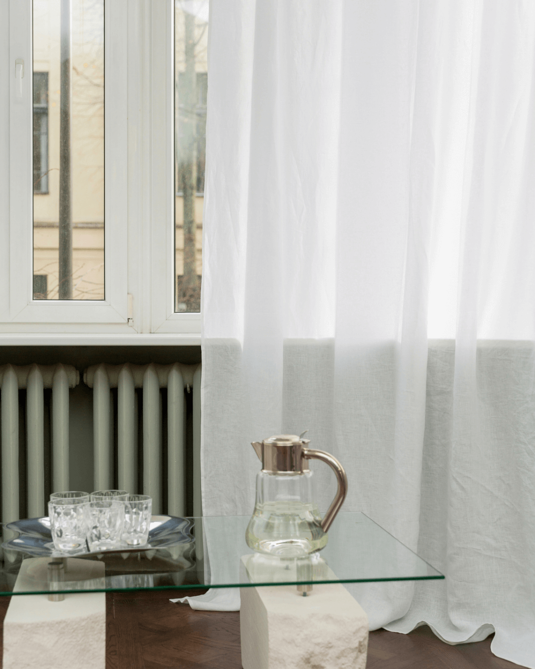 White semi-sheer linen curtains in room with glass table and pitcher